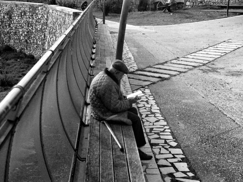 grayscale photo of man sitting on wooden bench