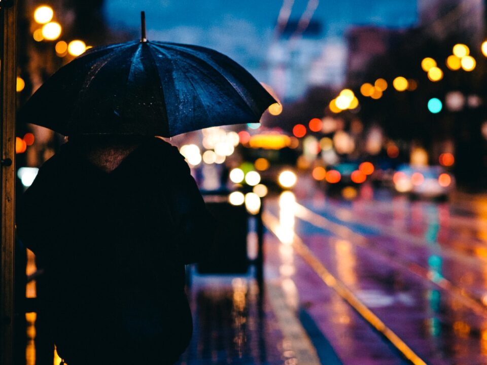 person walking on street while holding black umbrella near cars on road at nighttime