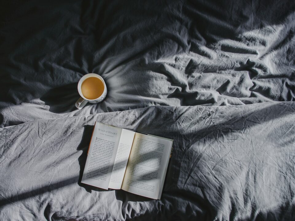 white ceramic mug beside book on gray textile