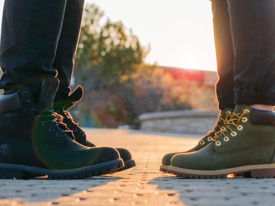 two people wearing green-and-black work boots standing on gray concrete pavement