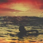 person swimming on body of water under red and orange sky