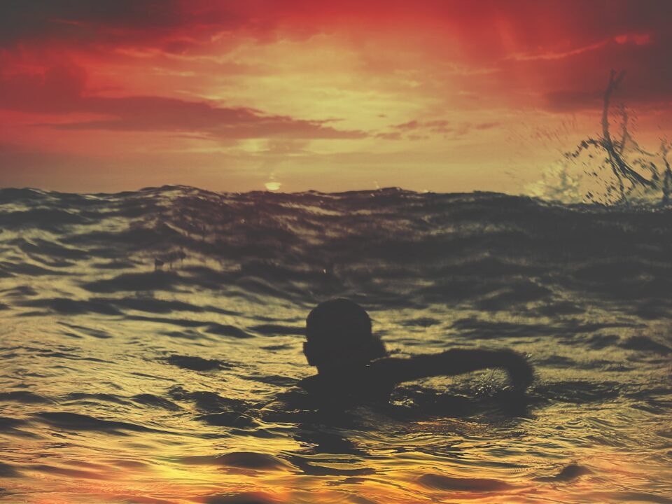 person swimming on body of water under red and orange sky