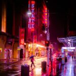 man in black jacket and blue denim jeans walking on street during night time