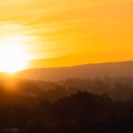 the sun is setting over the hills and trees