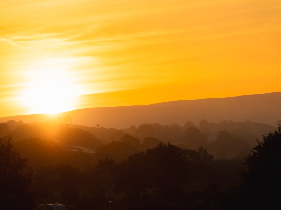the sun is setting over the hills and trees