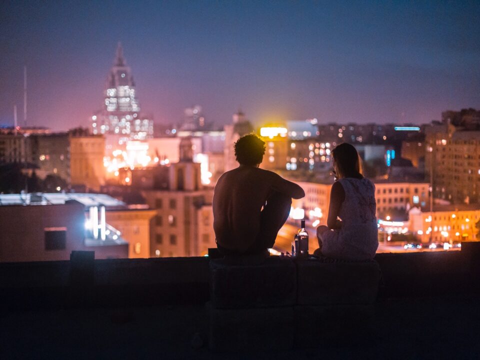 man and woman chilling on rooftop in front of high-rise buildings