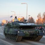 a military tank driving down a street next to a crowd of people