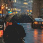 person walking on street and holding umbrella while raining with vehicle nearby