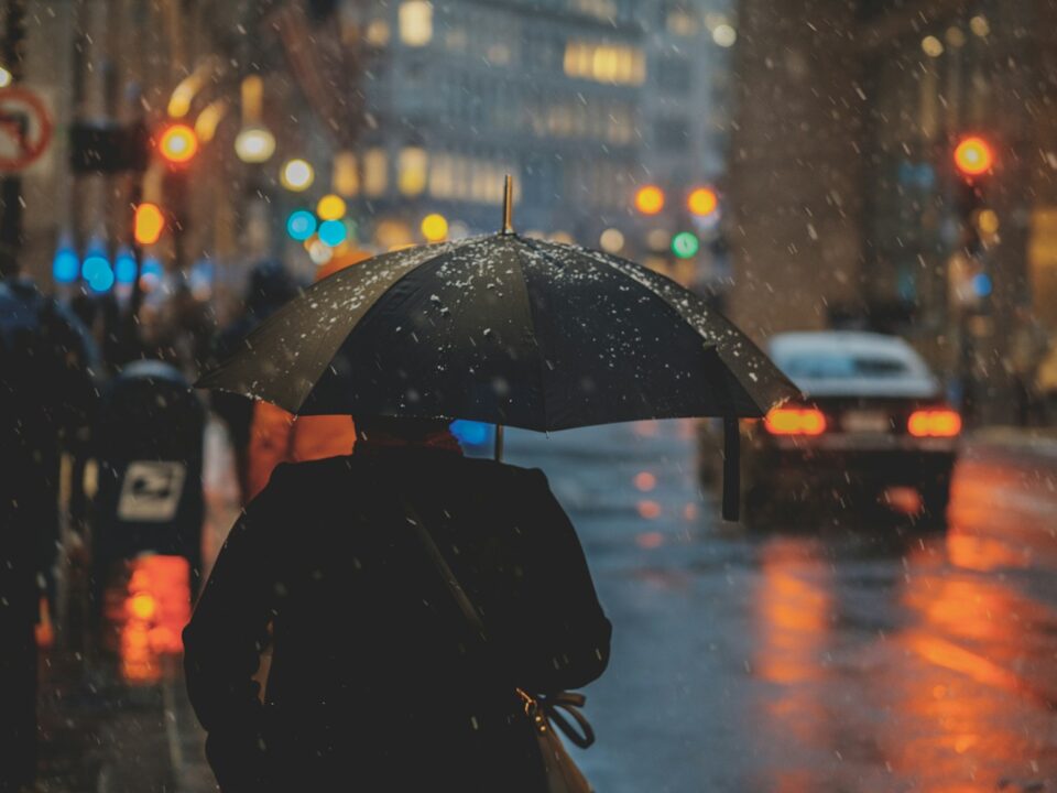 person walking on street and holding umbrella while raining with vehicle nearby