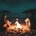 man and woman with bone fire sitting on seashore