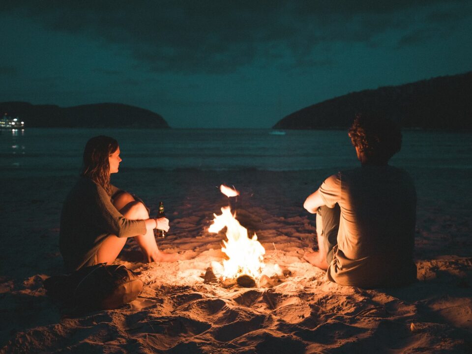 man and woman with bone fire sitting on seashore