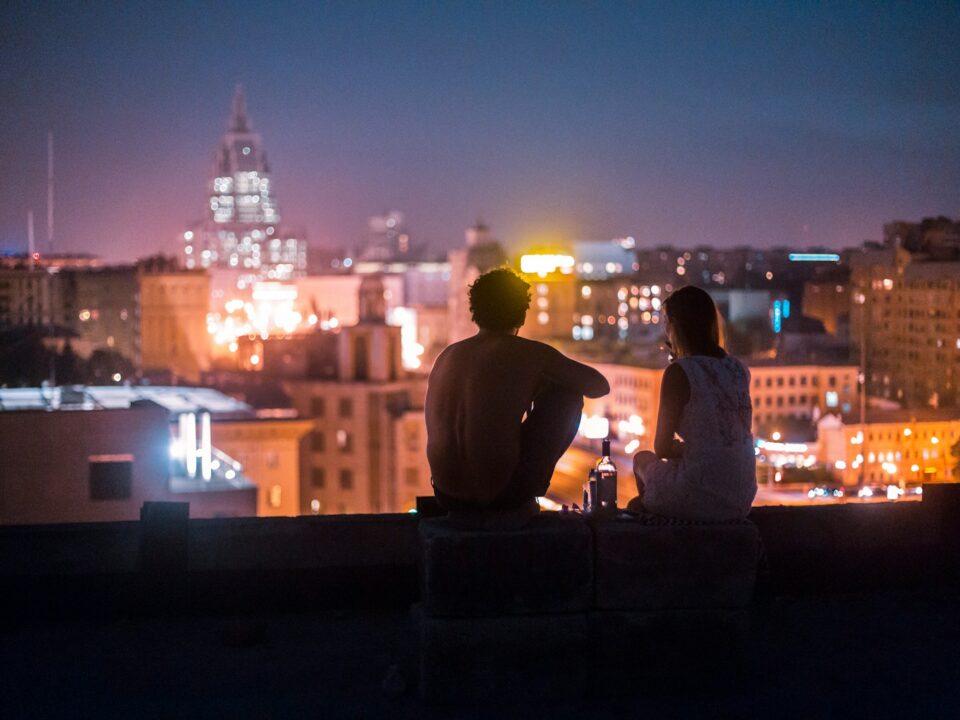 man and woman chilling on rooftop in front of high-rise buildings