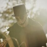 a man in a hat and coat walking through a field