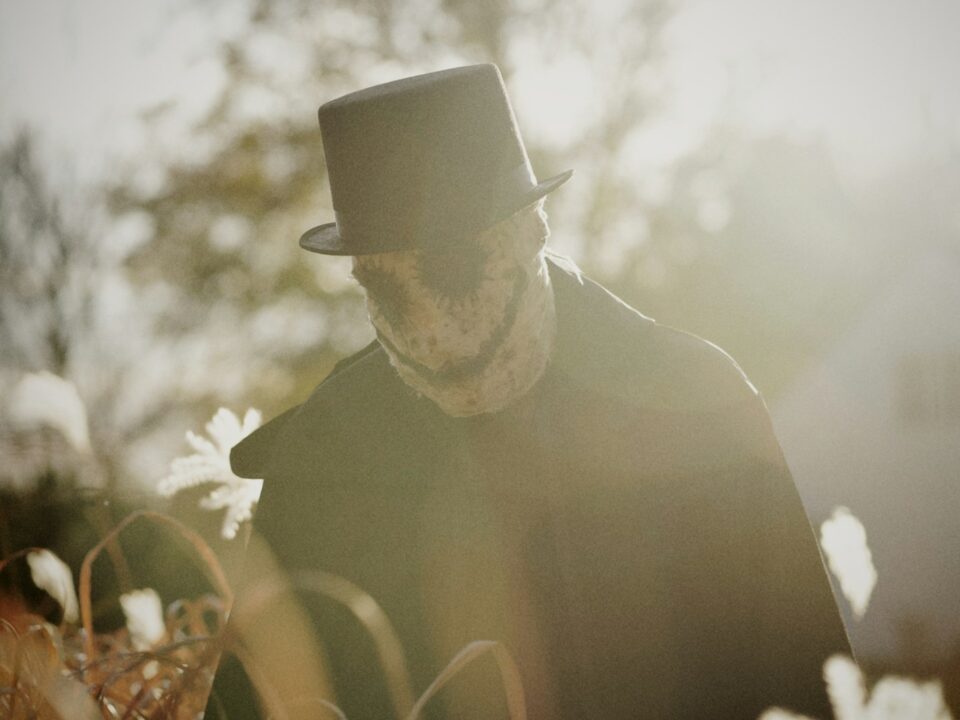 a man in a hat and coat walking through a field