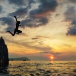 silhouette of man jumping on sea during sunset