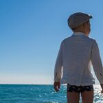 a little boy standing on a beach looking out at the ocean