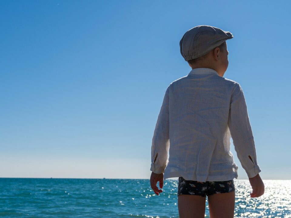 a little boy standing on a beach looking out at the ocean