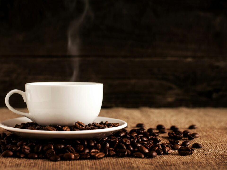 white ceramic mug and saucer with coffee beans on brown textile