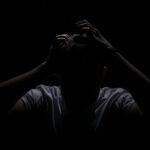 a man in the dark covering his face with his hands
