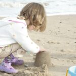 girl in white and pink polka dot jacket sitting on brown sand during daytime