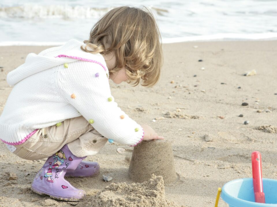 girl in white and pink polka dot jacket sitting on brown sand during daytime