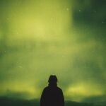 person standing under green aurora borealis