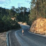 woman walking on gray asphalt road in between trees and rock formations