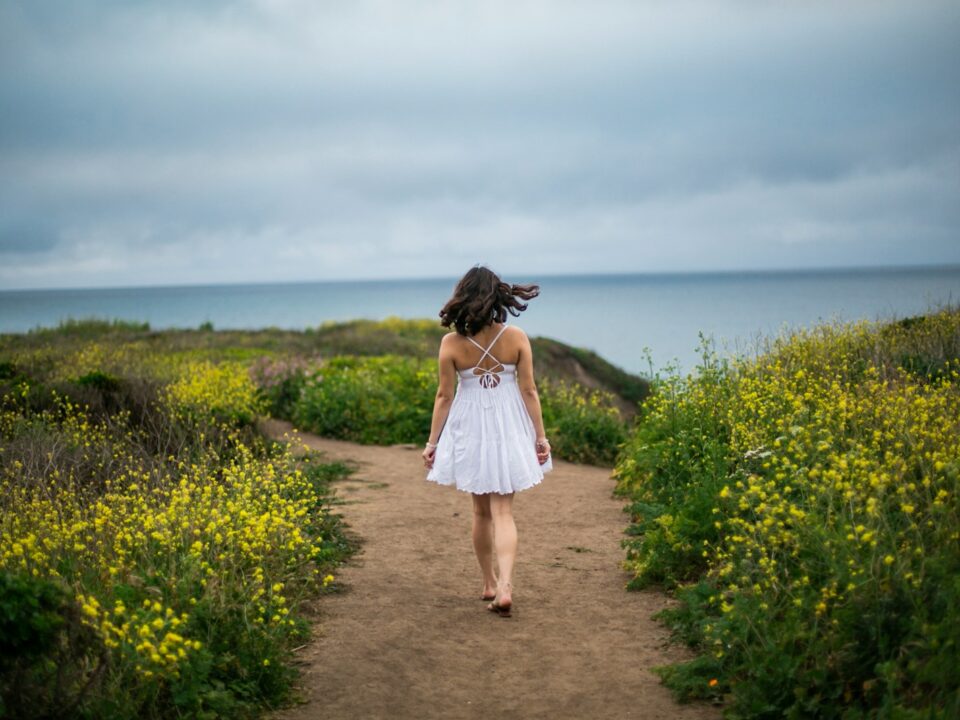 a woman in a white dress walking down a dirt path