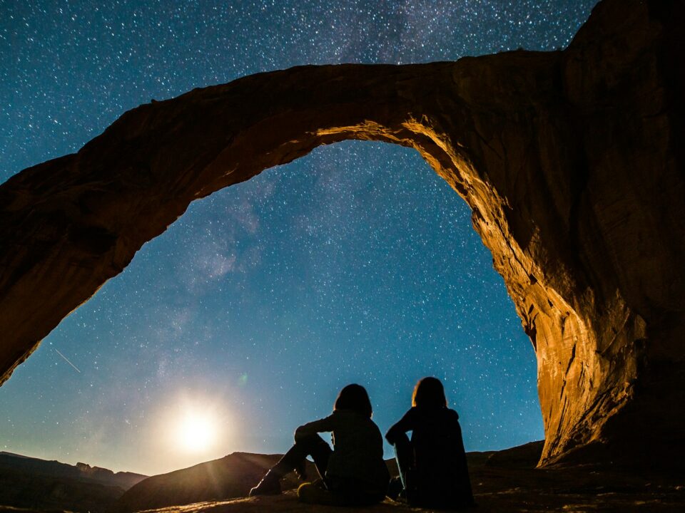 two person sitting under rock monolith