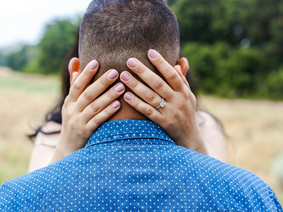 woman holding man's head near trees during daytime